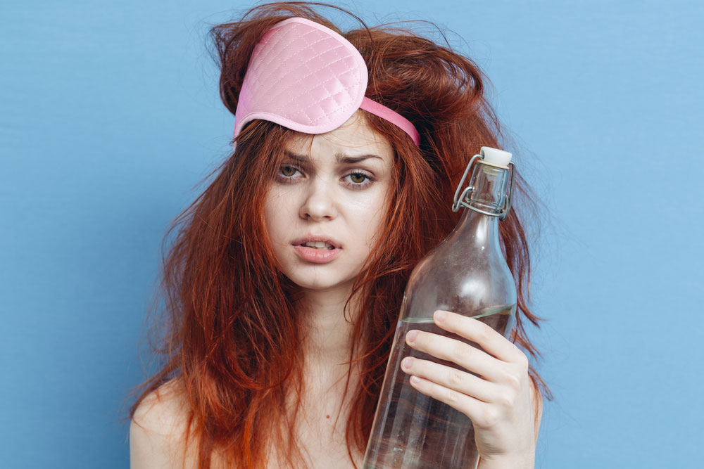 woman with messy hair and eye mask and water bottle