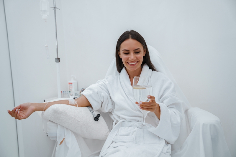 Beautiful woman in white bathrobe drinking water during iv infusion