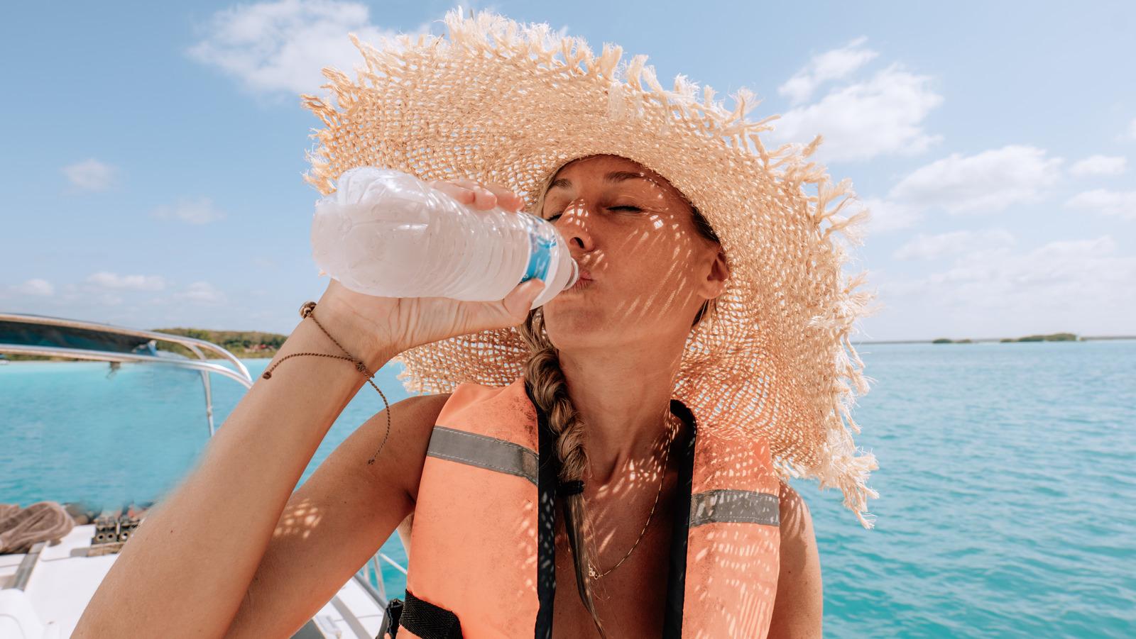 Woman in a straw hat and life vest drinking water from a bottle on a boat during a hot, sunny South Florida afternoon
